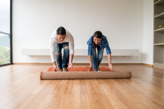 A man and a woman unroll a rug on a wood floor